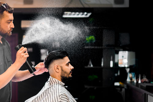 Homme coiffeur qui pulvérise un produit sur la tête d'un autre